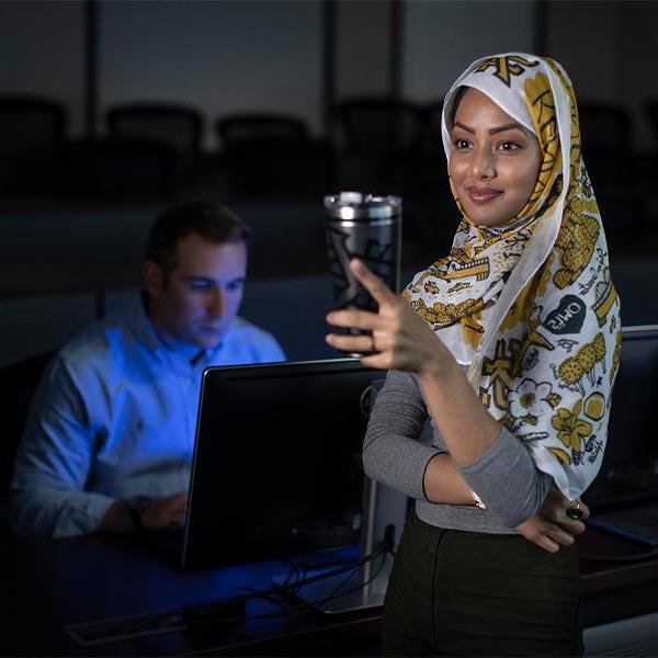 ksu student smiling for picture while a student in the background is using a laptop.